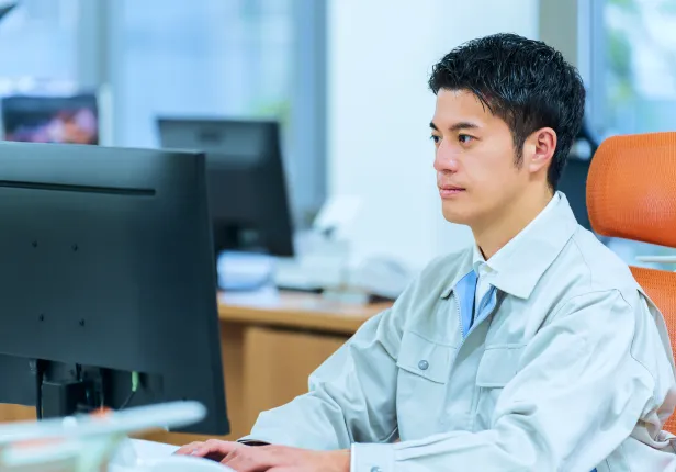 集中してPC作業をする作業着姿の男性。